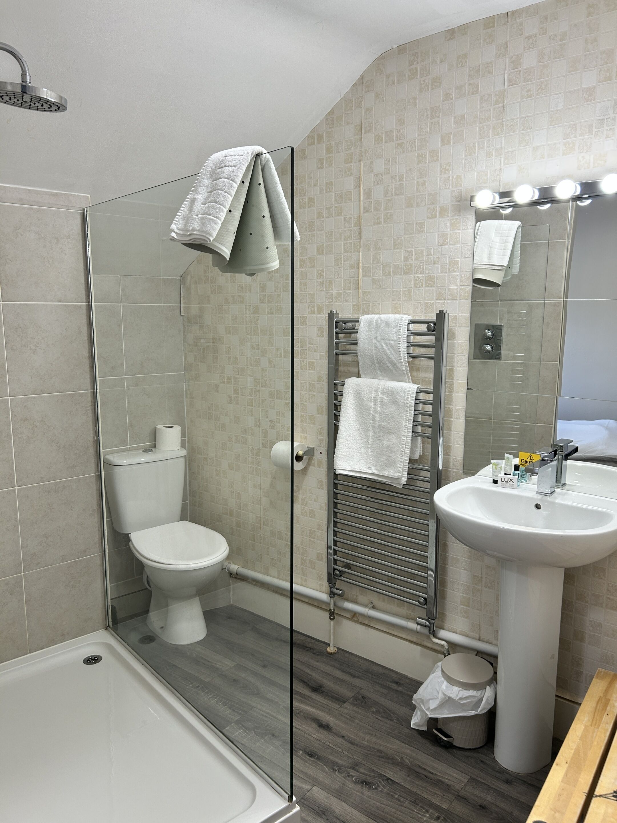 Un baño moderno con ducha envuelta en vidrio, inodoro, lavabo y espejo con luces.