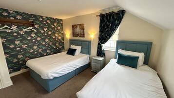Un dormitorio con dos camas, papel tapiz floral, una mesita de noche y un cuadro en la pared.