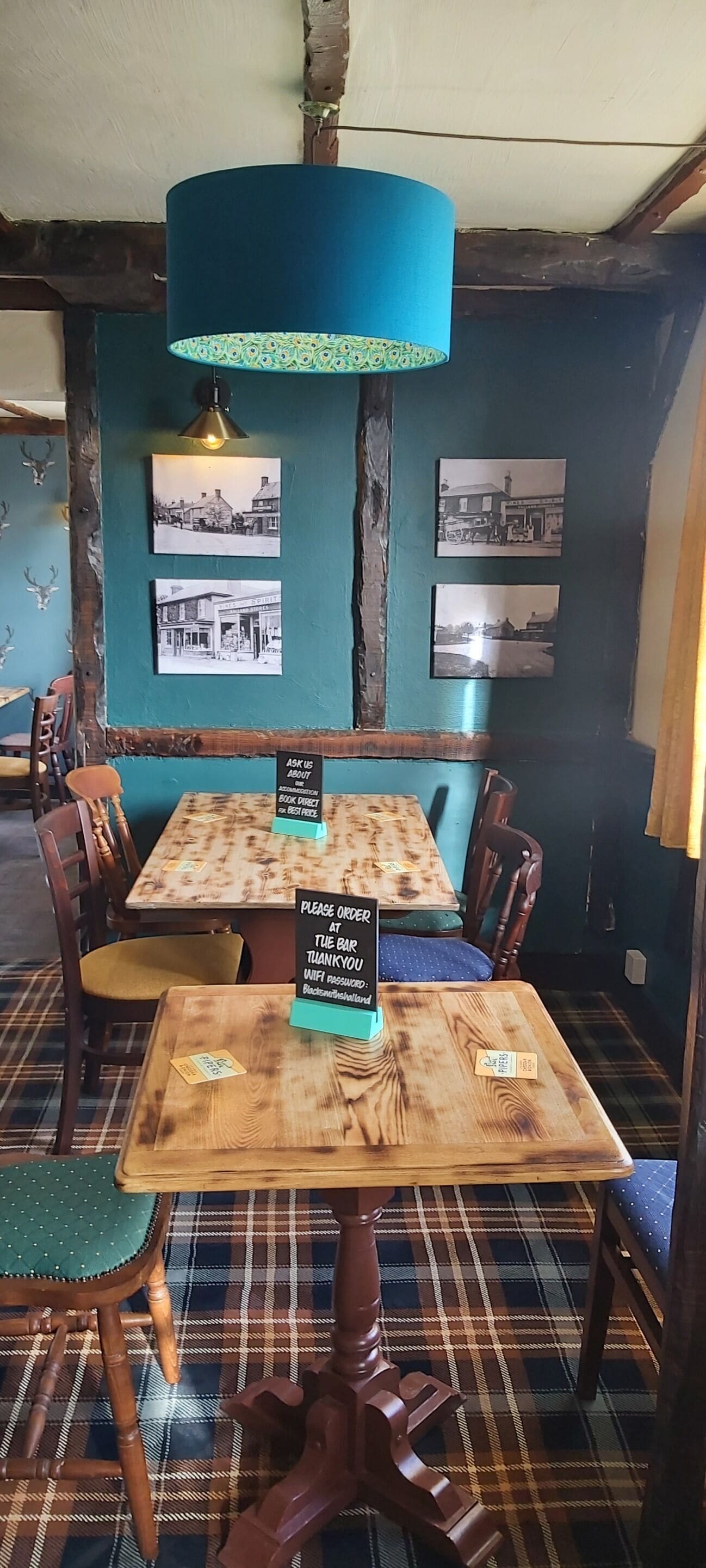 A rustic interior with wooden tables and chairs, a blue hanging lamp, and black-and-white photographs on the wall.