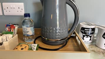A kitchen counter with a kettle, a water bottle, a mug, and a drawer containing snacks.