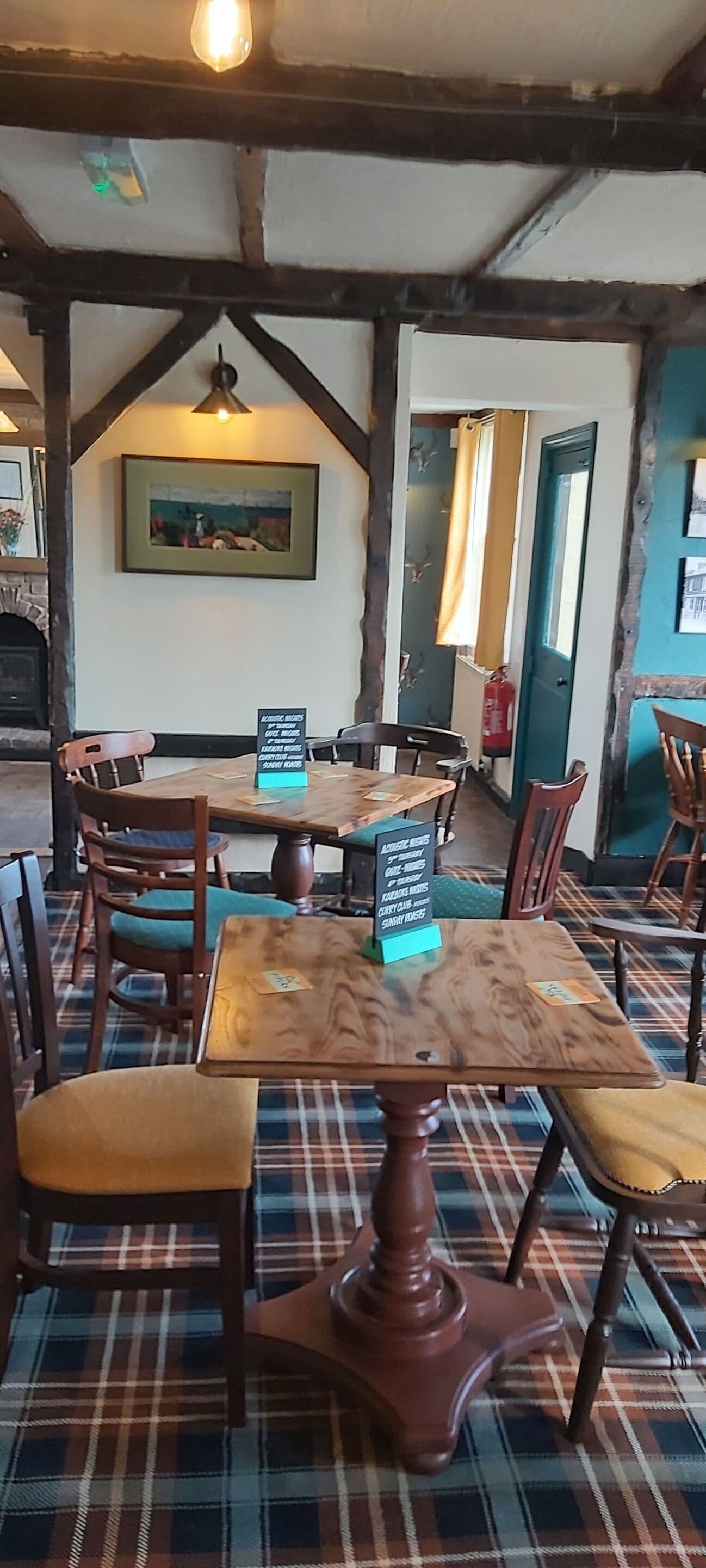 A cozy restaurant with wooden tables and chairs, a fireplace, and a painting on the wall.