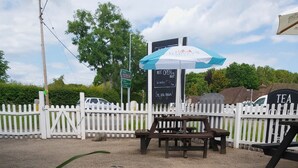 A picnic area with a white picket fence, a bench, and a table under a blue and white umbrella.