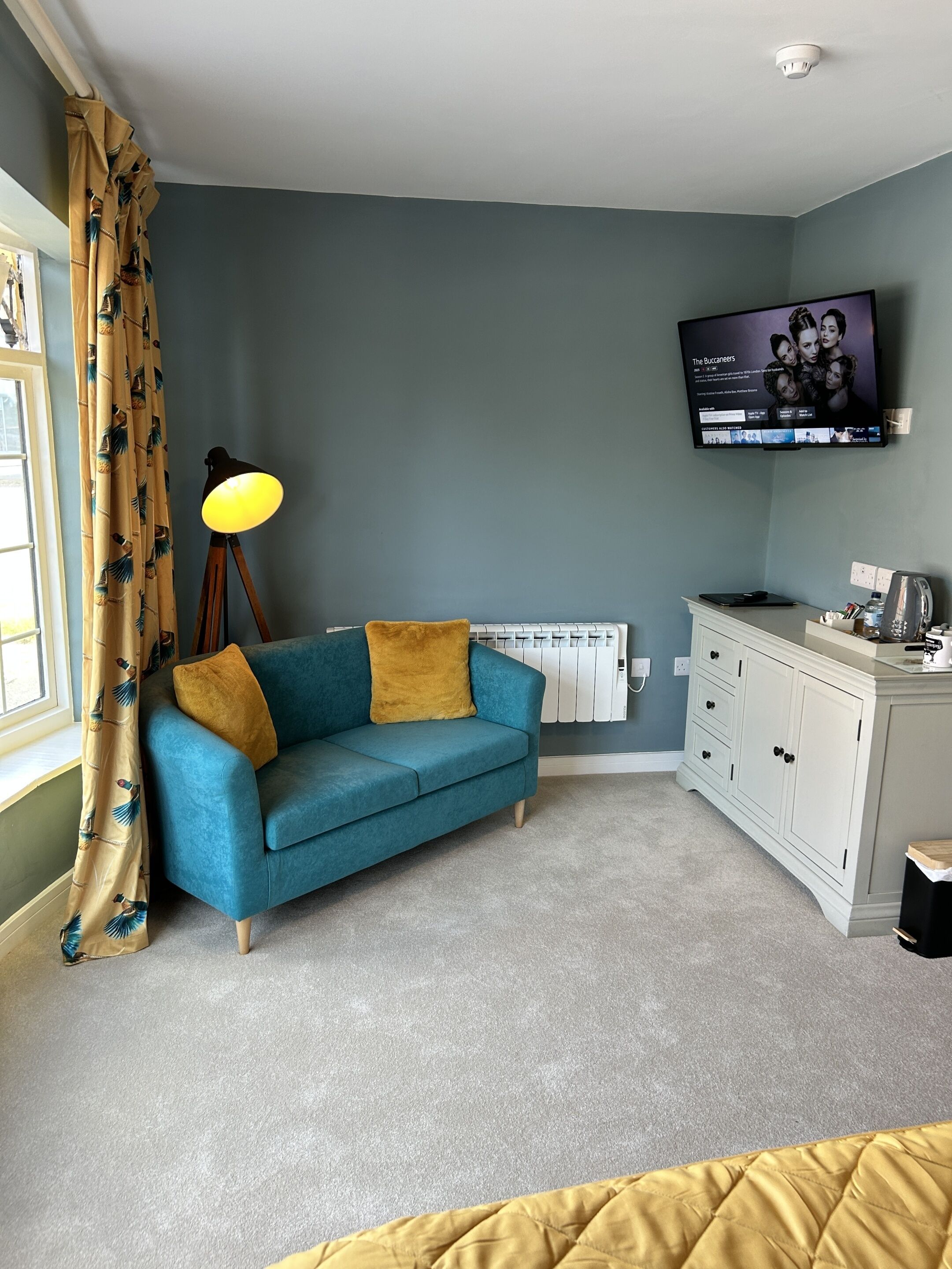 Una habitación con un sofá azul, una lámpara amarilla, un televisor en la pared y un armario blanco.