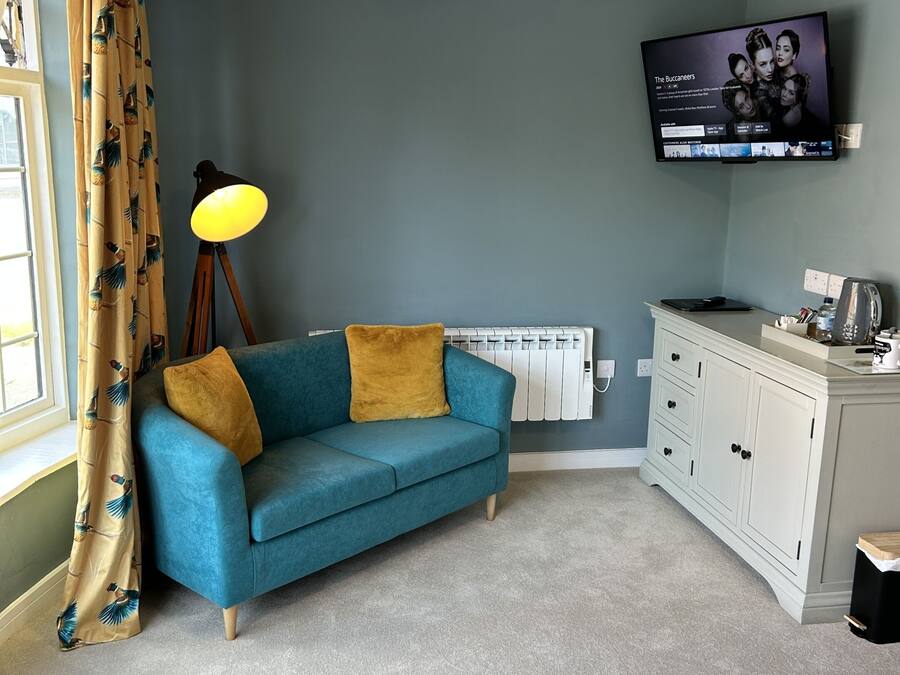 Una habitación con un sofá azul, una lámpara amarilla, un televisor en la pared y un armario blanco.