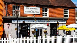A building with a sign for dining rooms and accommodation, a white picket fence, and outdoor umbrellas.