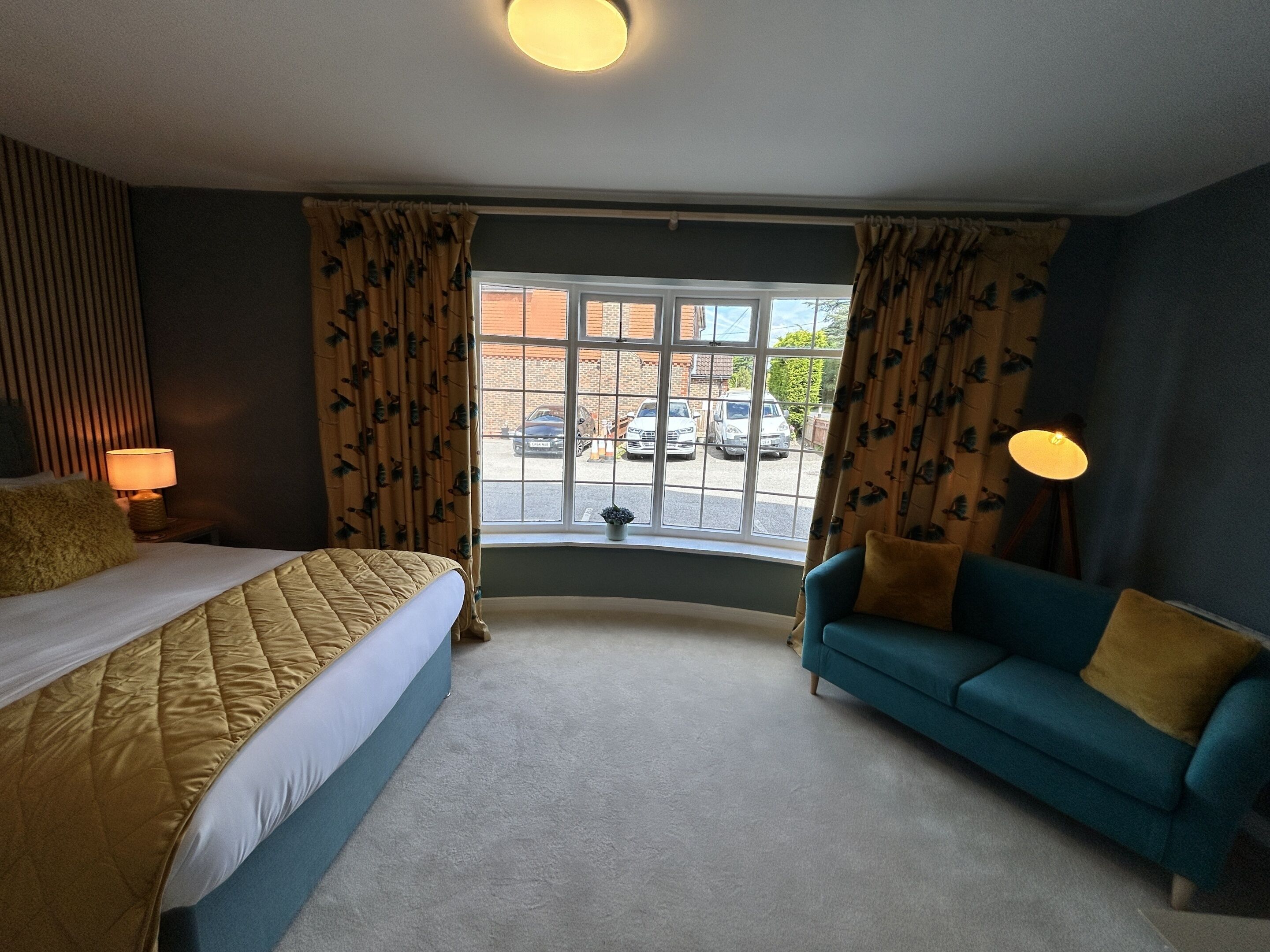 A hotel room with a bed, a sofa, a window with curtains, and two bedside lamps.