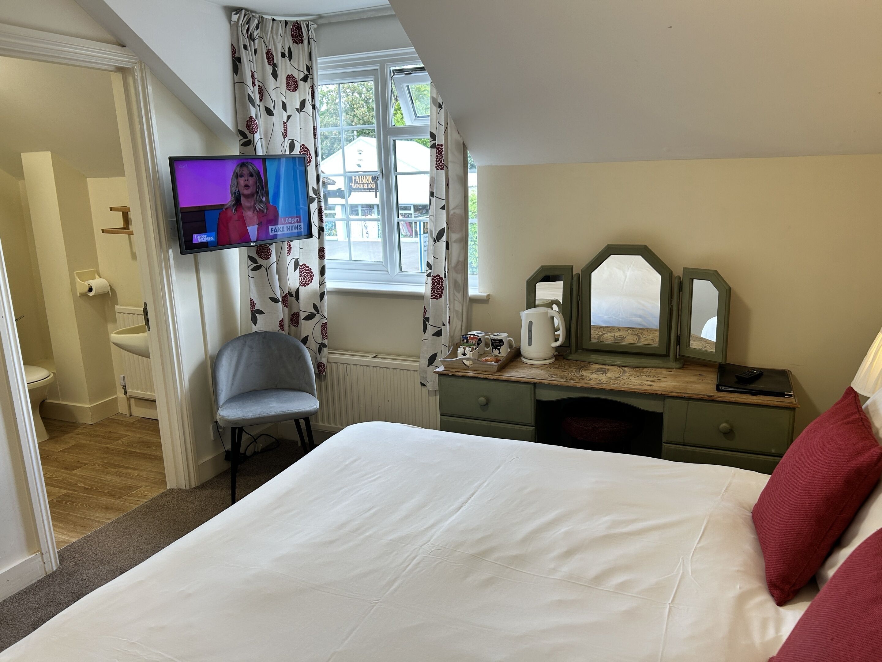A bedroom with a bed, a vanity with a mirror, a chair, a television, and a window with curtains.