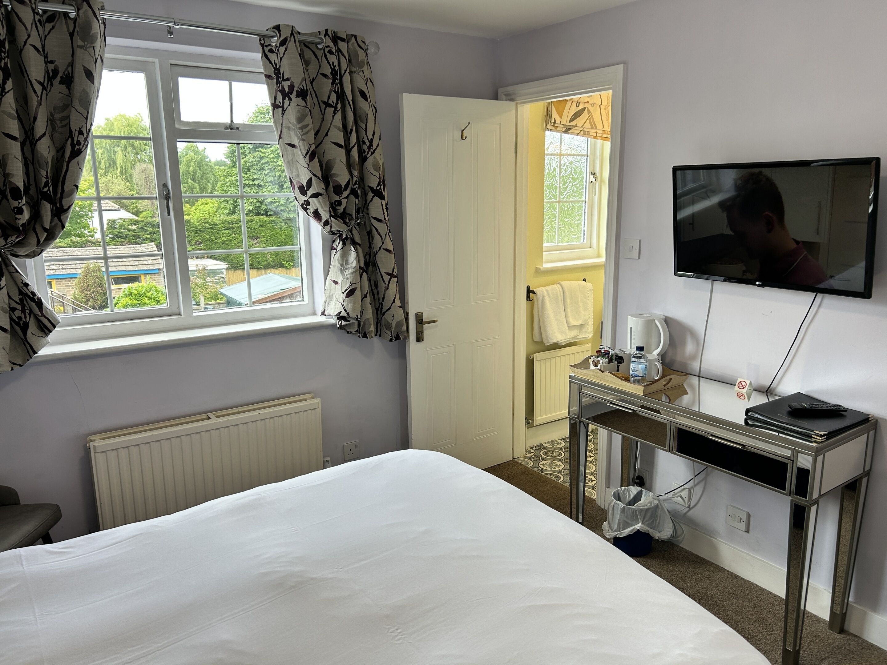 A hotel room with a bed, a desk with a coffee maker, a TV, and a window with curtains.