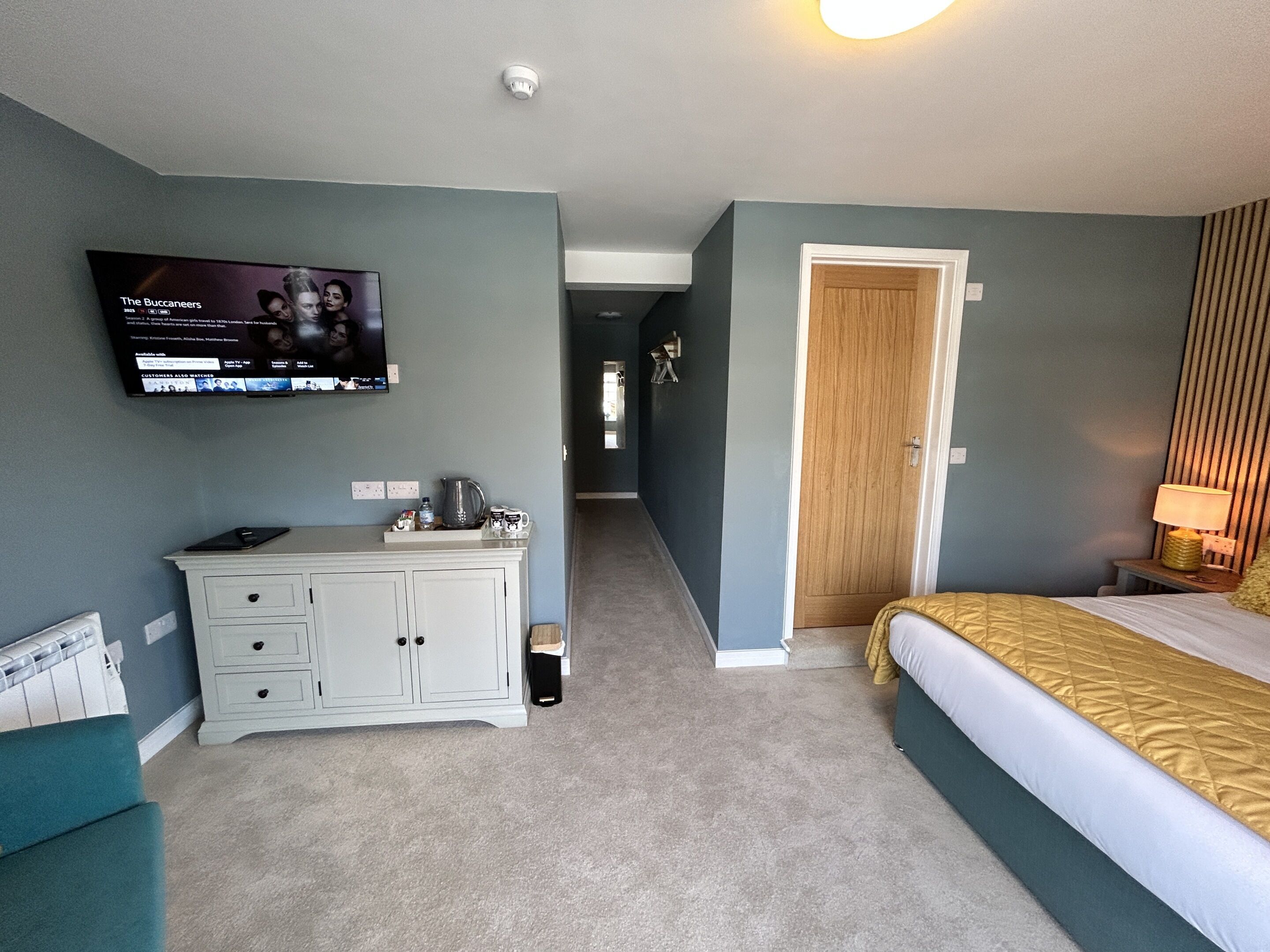 Una habitación de hotel con una cama, un escritorio con televisor, una puerta y una lámpara.
