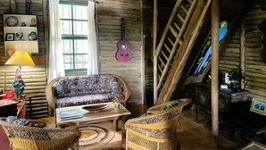 Un interior rústico de madera con un sofá, sillas de mimbre, una guitarra y una escalera.