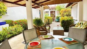 An outdoor patio with round glass tables, wicker chairs, and a variety of plants and flowers. - Villa 1 minute walking to beach with pool A/C pet friendly (Jaco)
