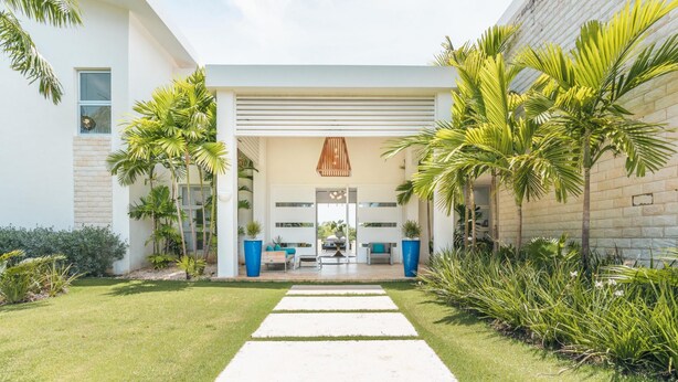 A modern building with a covered outdoor seating area, palm trees, and a clear sky.