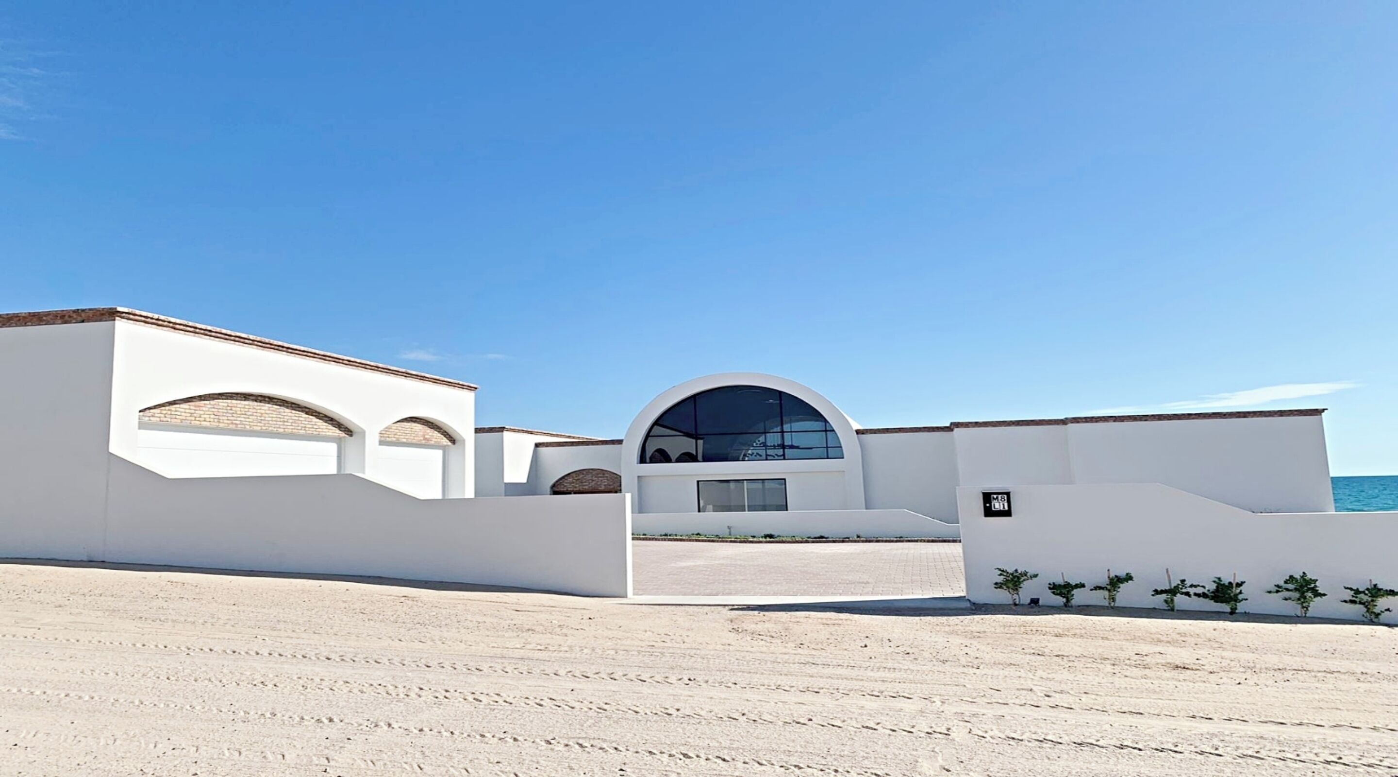 Un edificio moderno con una amplia entrada en arco, paredes blancas y una vista despejada del mar.