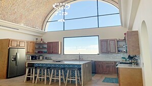 A modern kitchen with a large island, wooden cabinets, and a view through a large window.