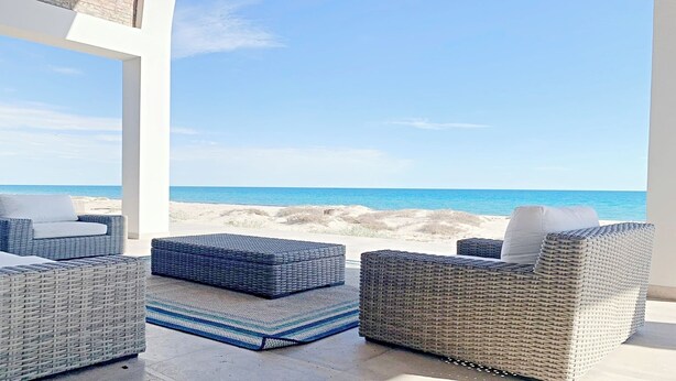 A beachside patio with wicker furniture and a view of the ocean.