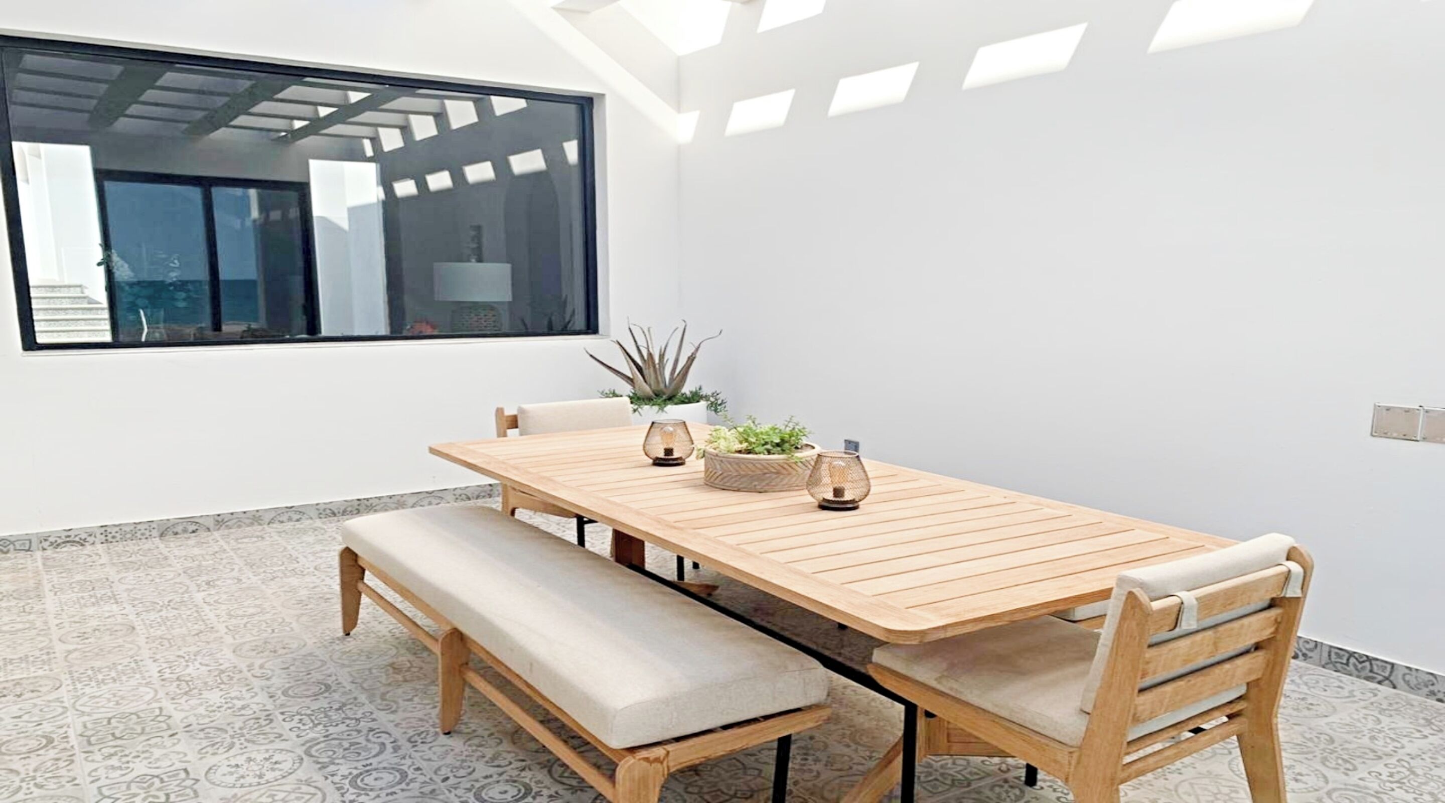 A modern dining area with a wooden table and benches, a large window, and a ceiling with skylights.