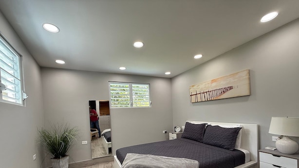 A modern bedroom with a bed, bedside table, lamp, and a painting on the wall. - EcoMar Rentals #4: Near Beach Couple's Tropical Retreat (Cabo Rojo)