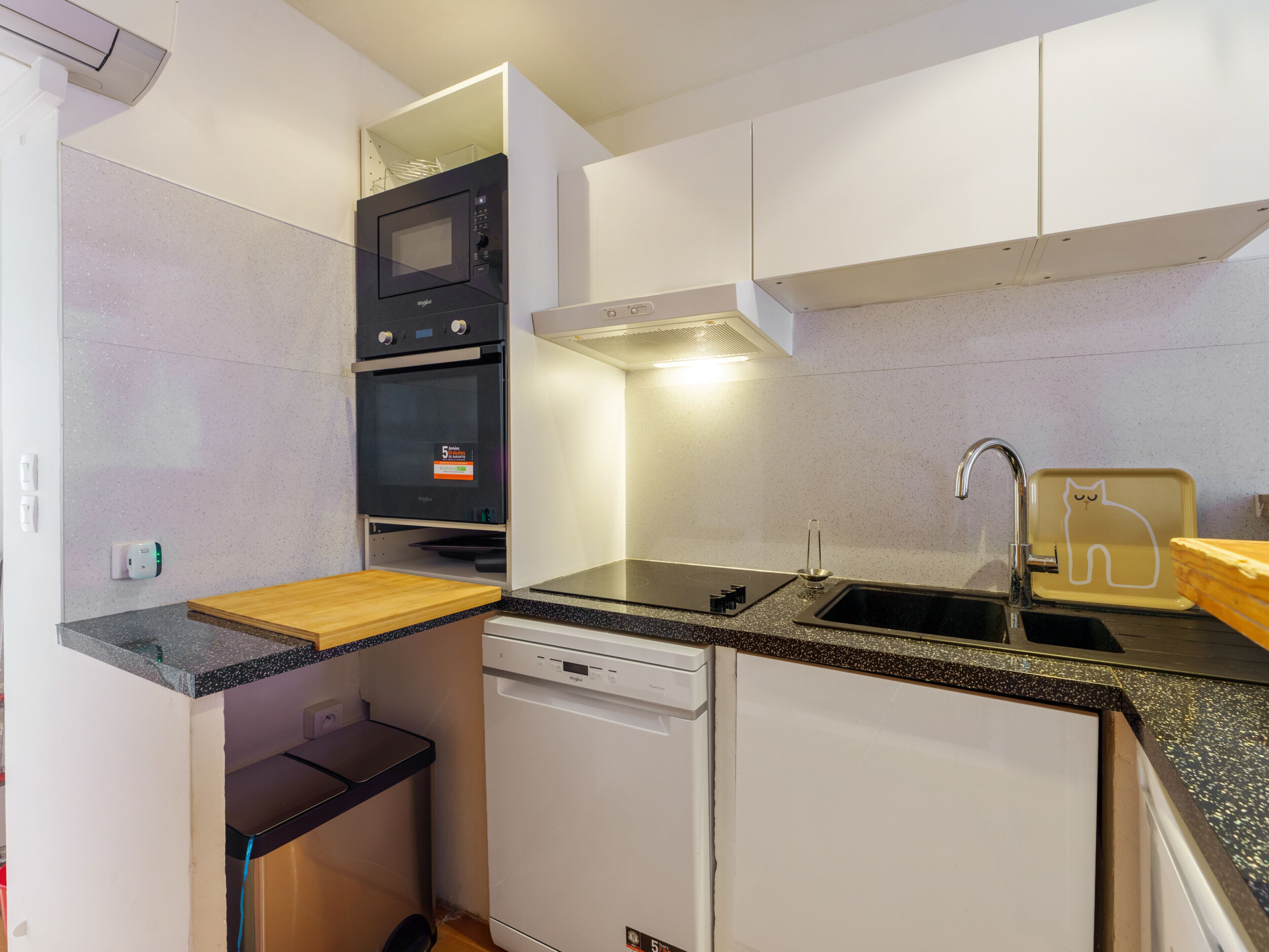 A compact kitchen with a microwave, oven, dishwasher, and a sink with a cat-shaped soap dish.