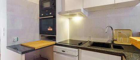 A compact kitchen with a microwave, oven, dishwasher, and a sink with a cat-shaped soap dish.