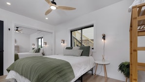 A bedroom with a large bed, a ceiling fan, a window with a view of a staircase, and a small side table. - Modern condo located in the resort village of Seven Devils. Great views! (Seven Devils)