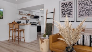 A modern living room with a brown sofa, wooden chairs, a coffee table, and a kitchen in the background. - Modern condo located in the resort village of Seven Devils. Great views! (Seven Devils)