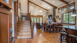 A spacious interior with a wooden staircase, a stone fireplace, and a dining area with multiple chairs and a bar. - Golf View, Hot Tub, Suncadia Pool Access (Cle Elum)