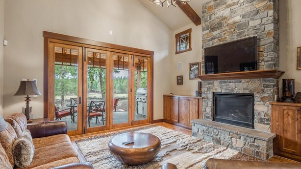 A spacious living room with a stone fireplace, leather sofas, and a large window offering a view of the outdoors. - Golf View, Hot Tub, Suncadia Pool Access (Cle Elum)