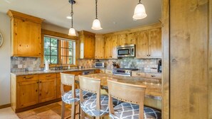 A kitchen with wooden cabinets, a stone backsplash, and a central island with bar stools. - Family Friendly w/ Suncadia Pool Access (Cle Elum)