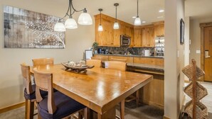 A dining area with a wooden table and chairs, a chandelier, and a kitchen in the background. - Pet Friendly Condo, Suncadia Pool Access (Cle Elum)