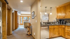 A kitchen with wooden cabinets, a dishwasher, and a dining area with a chair. - Pet Friendly Condo, Suncadia Pool Access (Cle Elum)