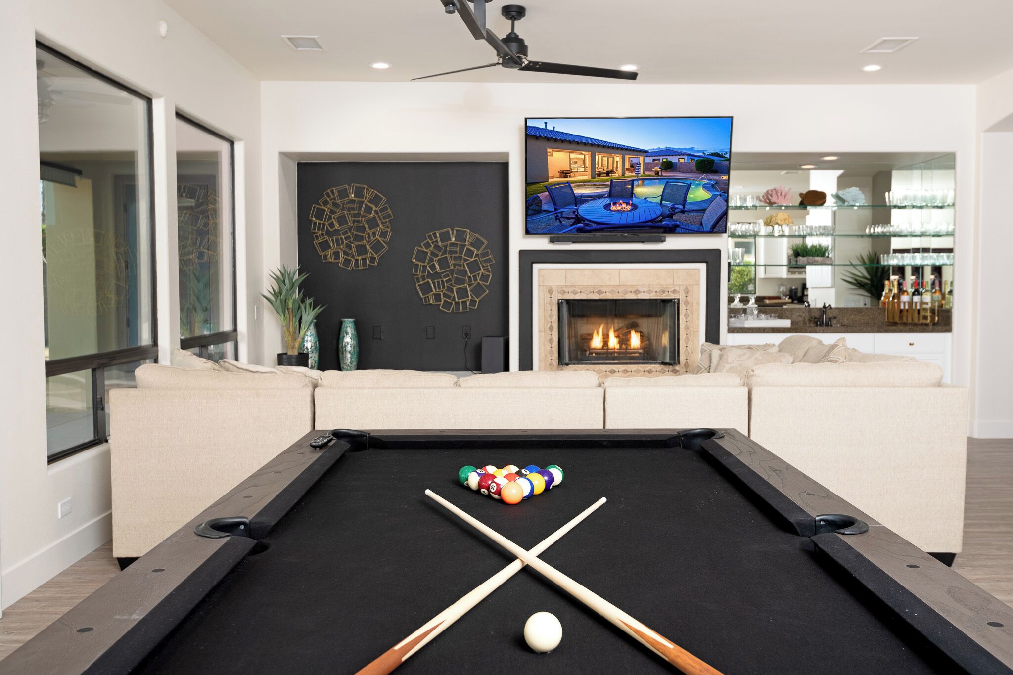 Une table de billard dans un salon, avec un téléviseur au-dessus, une cheminée et un coin bar à l’arrière-plan.