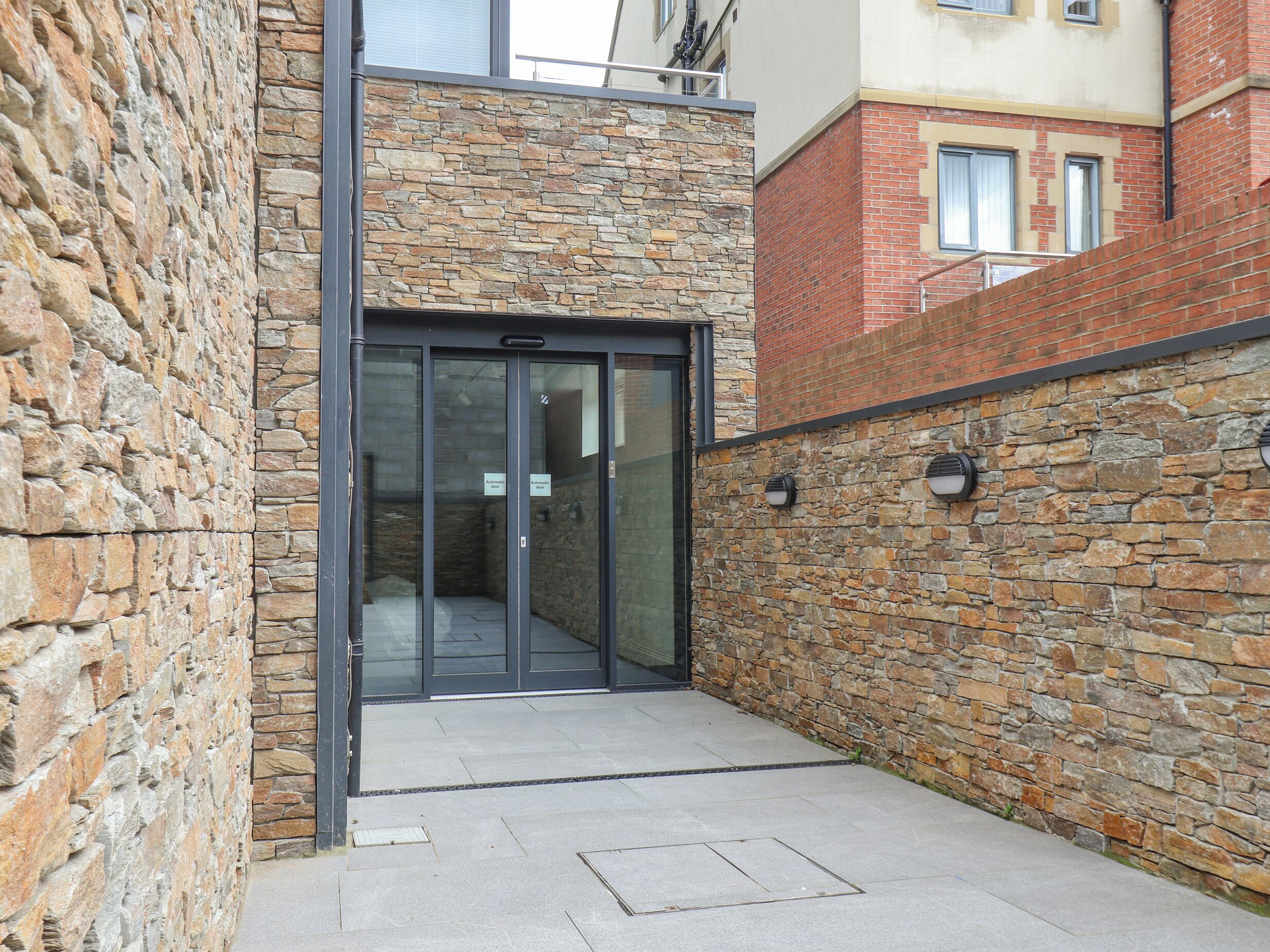 A stone facade with a modern glass door entrance, a metal staircase, and a brick wall.