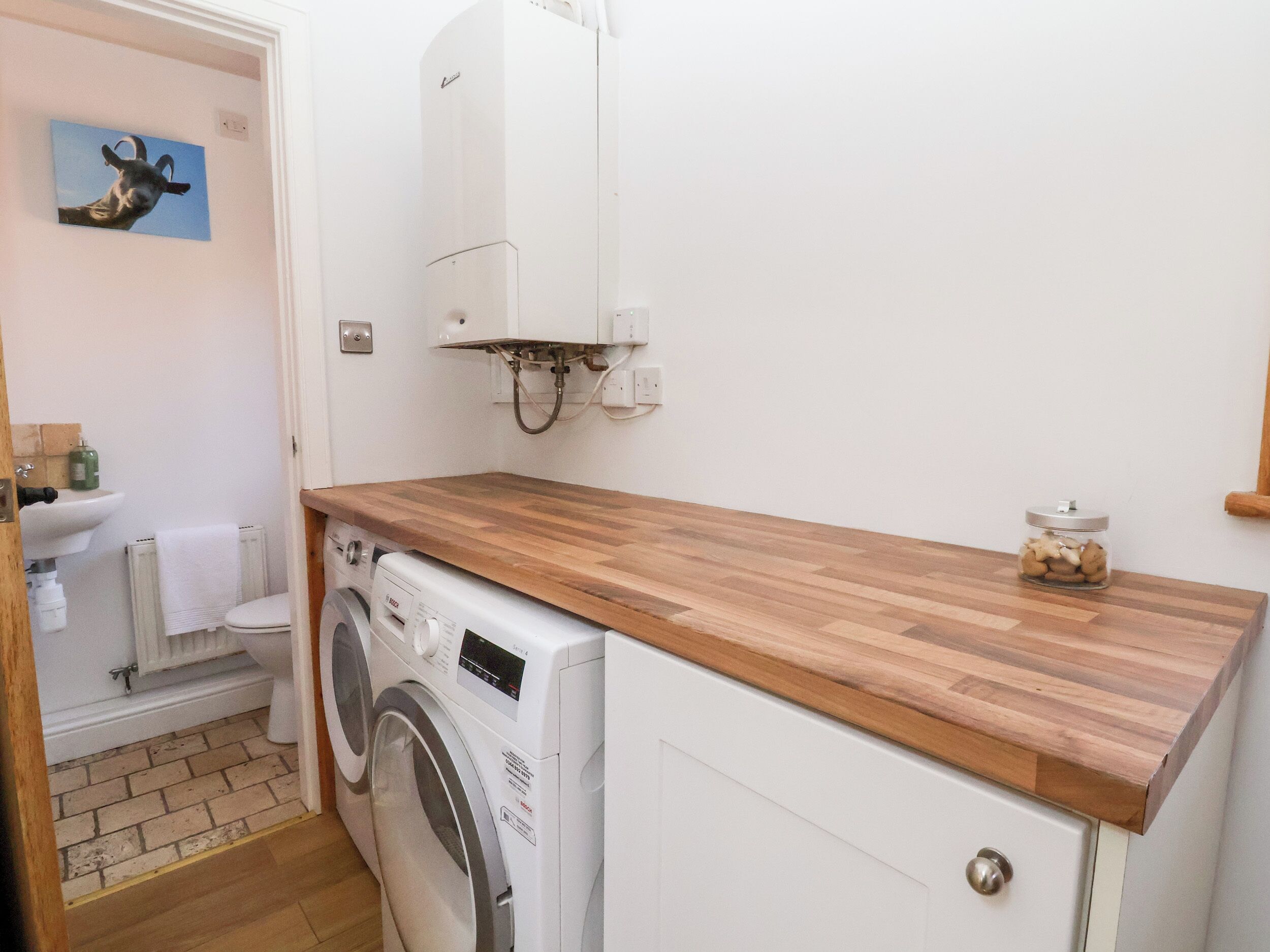 Une petite buanderie équipée d’un lave-linge, d’un évier et d’un plan de travail en bois.