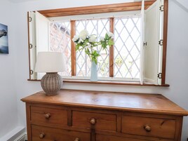 A wooden dresser with a white vase containing white flowers and a lamp, positioned in front of a window with open shutters.