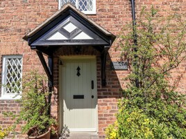 A brick building with a white door, a black and white gable, and a sign reading "JASMIN COTTAGE".