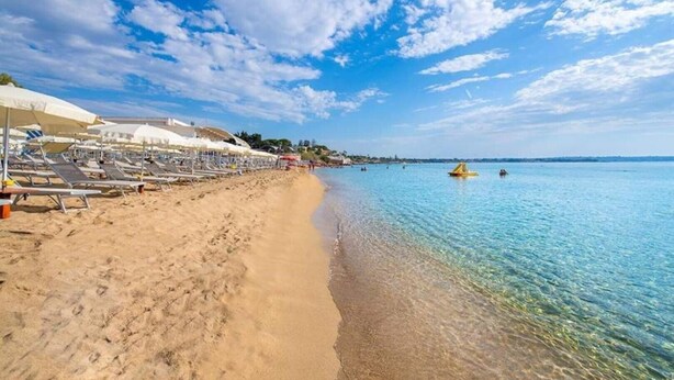 A beach with sun loungers and umbrellas, clear blue water, and a sandy shore. - Syracuse sea (Arenella)