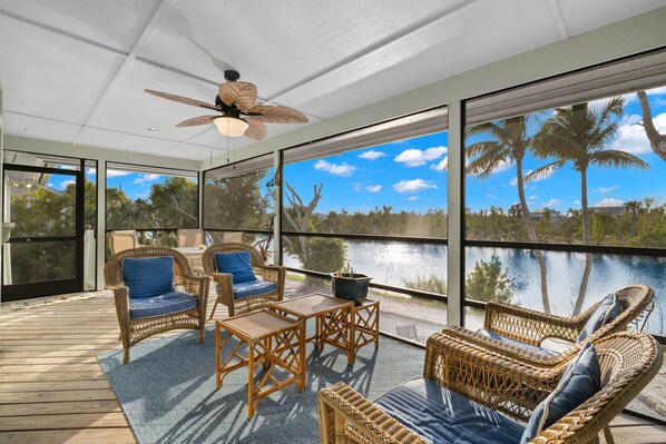 Enjoy expansive views of the water and palm trees from the comfort of this room, featuring a ceiling fan and wicker furniture.