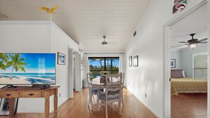 Comedor con mesa y sillas de madera, televisor sobre un mueble y vistas al exterior a través de una puerta corrediza.