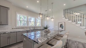 A modern kitchen with a large island, bar stools, and pendant lighting. - 30A Brand NEW 4 Bedroom-8 Bikes-LARGE POOL-Turf yard Close to Beach-Golf Cart! (Santa Rosa Beach)