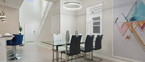 Un comedor moderno con una mesa de cristal, sillas negras y una lámpara de araña.