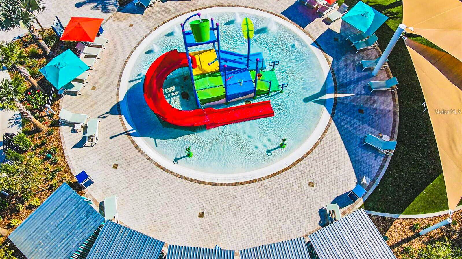 A circular water play area with slides and a ladder, surrounded by lounge chairs and umbrellas.