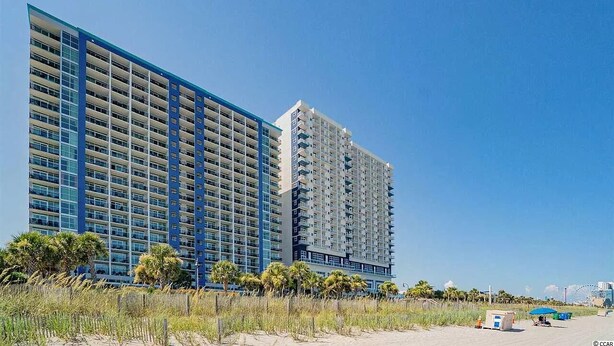 A high-rise hotel with multiple balconies, located near a beach with palm trees and a clear sky. - Ocean Front 3 Bedroom, BAY VIEW Resort, 7th Floor, 12 Guests (Myrtle Beach)