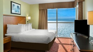 A hotel room with a bed, a desk, a TV, a window with a view of the sea, and a painting on the wall. - Ocean Front 3 Bedroom, BAY VIEW Resort, 7th Floor, 12 Guests (Myrtle Beach)