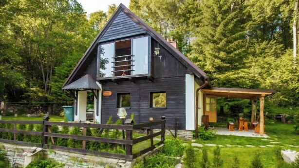 Una casa moderna con facciata scura, un patio in legno e un vialetto in pietra che conduce all'ingresso.