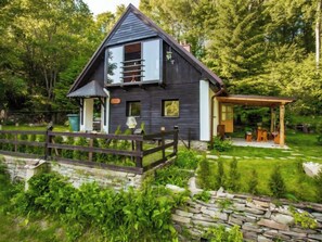 Une maison moderne à l’extérieur sombre, dotée d’une terrasse en bois et d’un chemin de pierre menant à l’entrée.