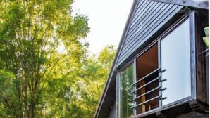 Una casa moderna con facciata scura, un balcone ben visibile e un giardino curato con due poltrone e un tavolino.