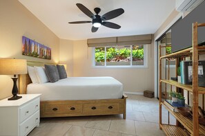 Relax in comfort with a large bed under a ceiling fan, surrounded by lush views and a bookshelf.