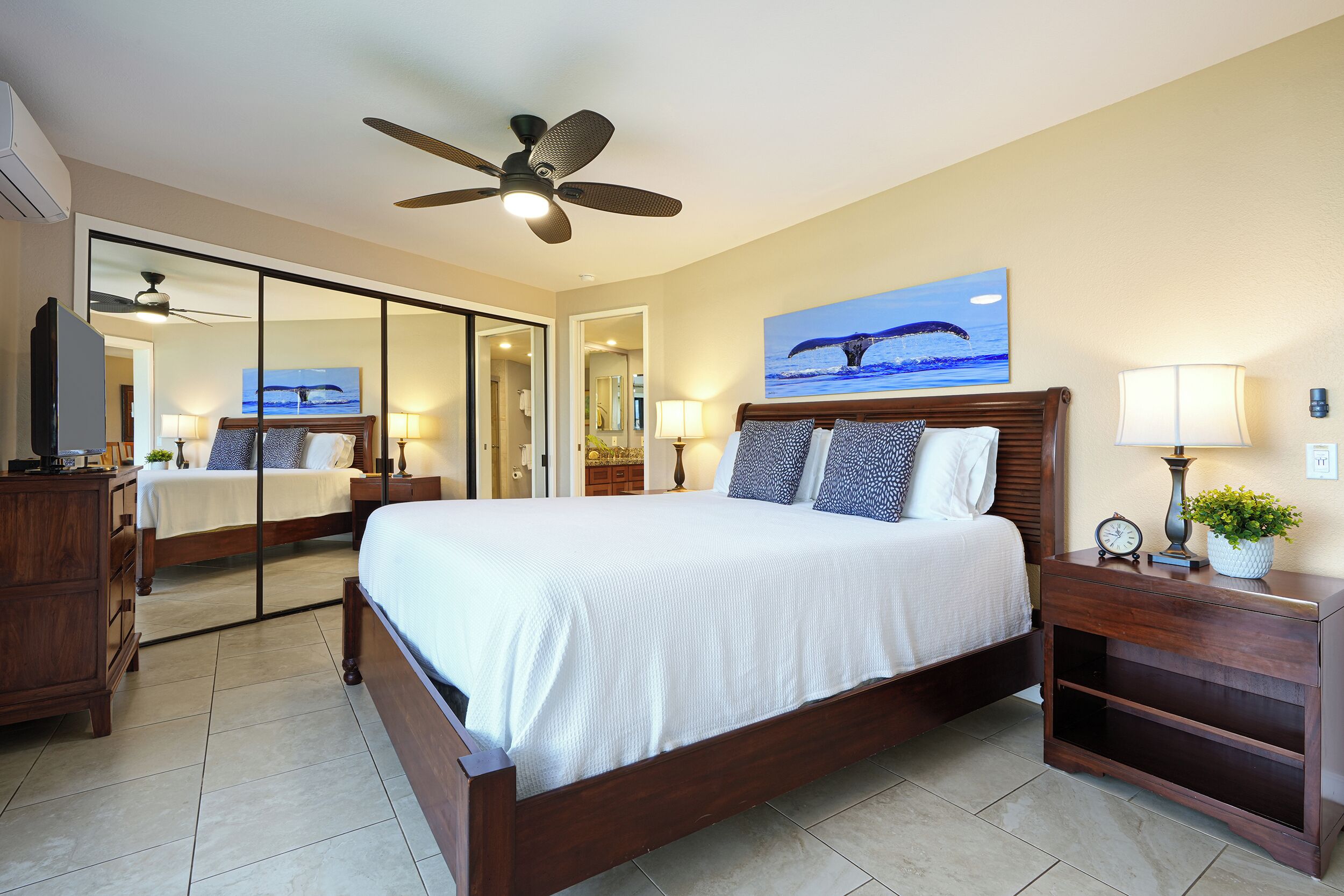 A spacious bedroom with a large bed, a ceiling fan, a nightstand with a clock, and a wall-mounted TV.