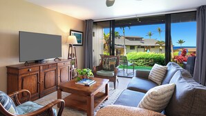 A modern living room with a flat-screen TV, wooden furniture, a ceiling fan, and a view of the ocean.