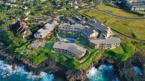 An aerial view of a coastal resort with multiple buildings, a swimming pool, and a rocky shoreline.